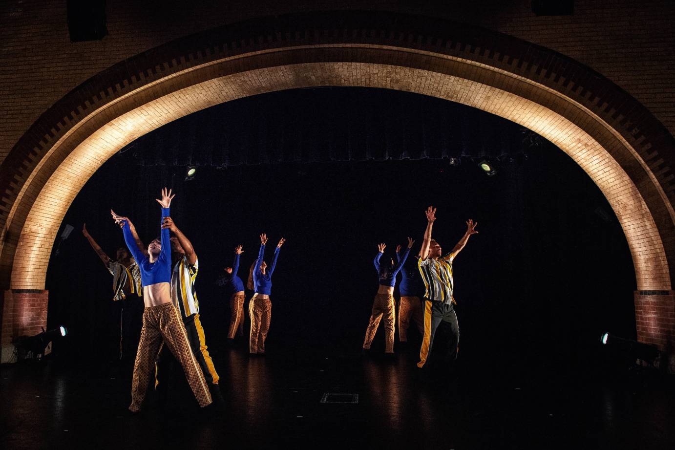 Dancers facing outward in a circle raise their arms high